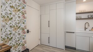 Ett modernt kök med vita skåp, ett träbord och en blommig tapet på en av väggarna.