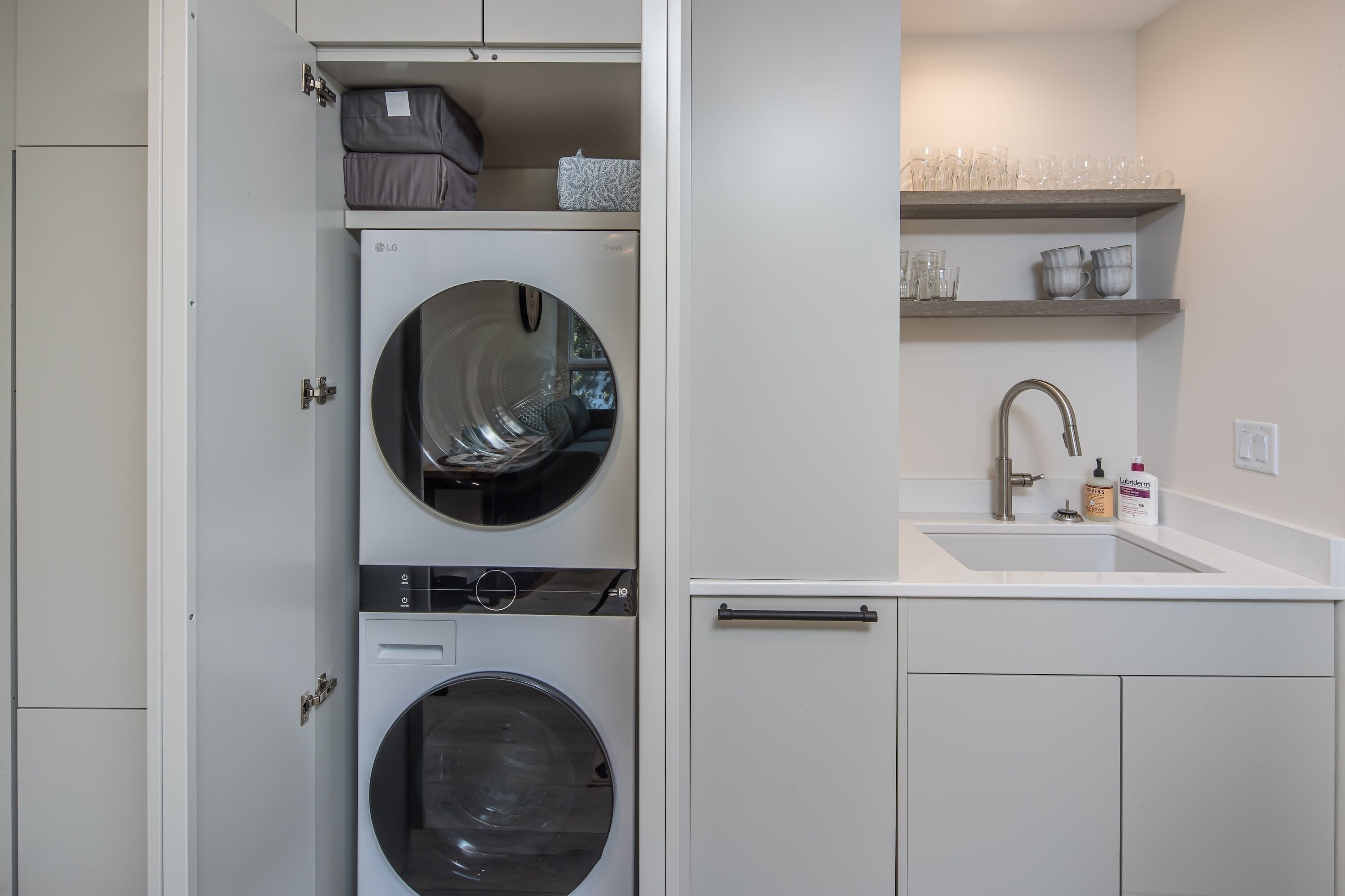 Un área de lavandería compacta con dos lavadoras, un lavabo y estantes de almacenamiento.