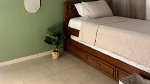 A bedroom with a bed, a wooden headboard, a green wall, and a potted plant.