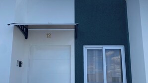 A white door with a number "12" above it, a small window with a white frame, and a dark green wall to the right.