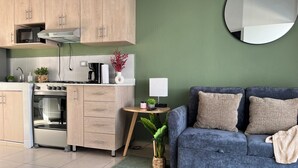 A modern kitchen with wooden cabinets, a built-in oven, and a microwave. There's a round mirror on the wall and a blue sofa with cushions.