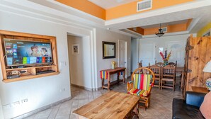A living room with a wooden coffee table, a colorful striped chair, a black leather sofa, and a television mounted on the wall. - Delphin 103, Las Palmas Resort (Puerto Peñasco)