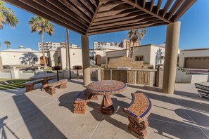 An outdoor patio with a round table, two benches, and a bar area. - Grande 105, Las Palmas Resort (Puerto Peñasco)