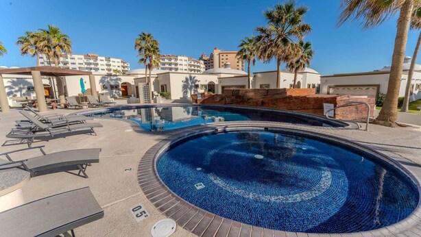 A swimming pool with lounge chairs and palm trees, surrounded by buildings. - Grande 105, Las Palmas Resort (Puerto Peñasco)