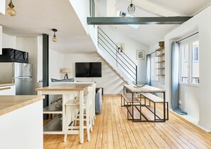 Ett modernt kök med en inbyggd mikrovågsugn, en matplats med ett träbord och vita stolar, en trappa med ett metallräcke och ett stort fönster med utsikt.