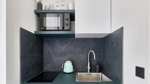 A compact kitchen with a microwave, kettle, and stainless steel sink. - Bastille · 11th · Stylish & Quiet Studio – managed by Mey Agency (Paris)