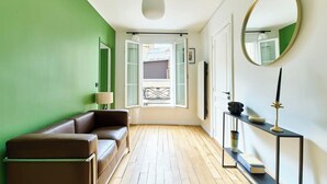 A room with a green wall, a brown leather sofa, a wooden floor, a round mirror, and a small table with a lamp. - Bastille · 11th · Stylish & Quiet Studio – managed by Mey Agency (Paris)