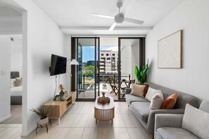 Una sala de estar moderna con un sofá gris, una mesa de centro, un televisor y un balcón con vistas a edificios.