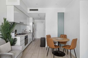Una cocina moderna con armarios blancos, una zona de comedor con una mesa redonda y cuatro sillas, y un sofá gris.