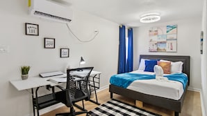 A modern bedroom with a bed, desk, chair, and a wall-mounted air conditioner. - Stroll to the Dome Sleek 1BR Near Downtown (San Antonio)
