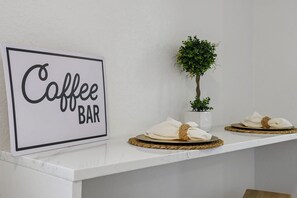 A sign reading "Coffee BAR" on a white wall, with a small potted plant and two woven placemats with napkins on a white counter. - Stroll to the Dome Sleek 1BR Near Downtown (San Antonio)