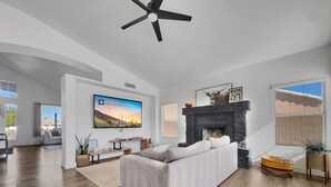 Un ampio soggiorno con camino, una grande TV a schermo piatto e una ventola a soffitto.