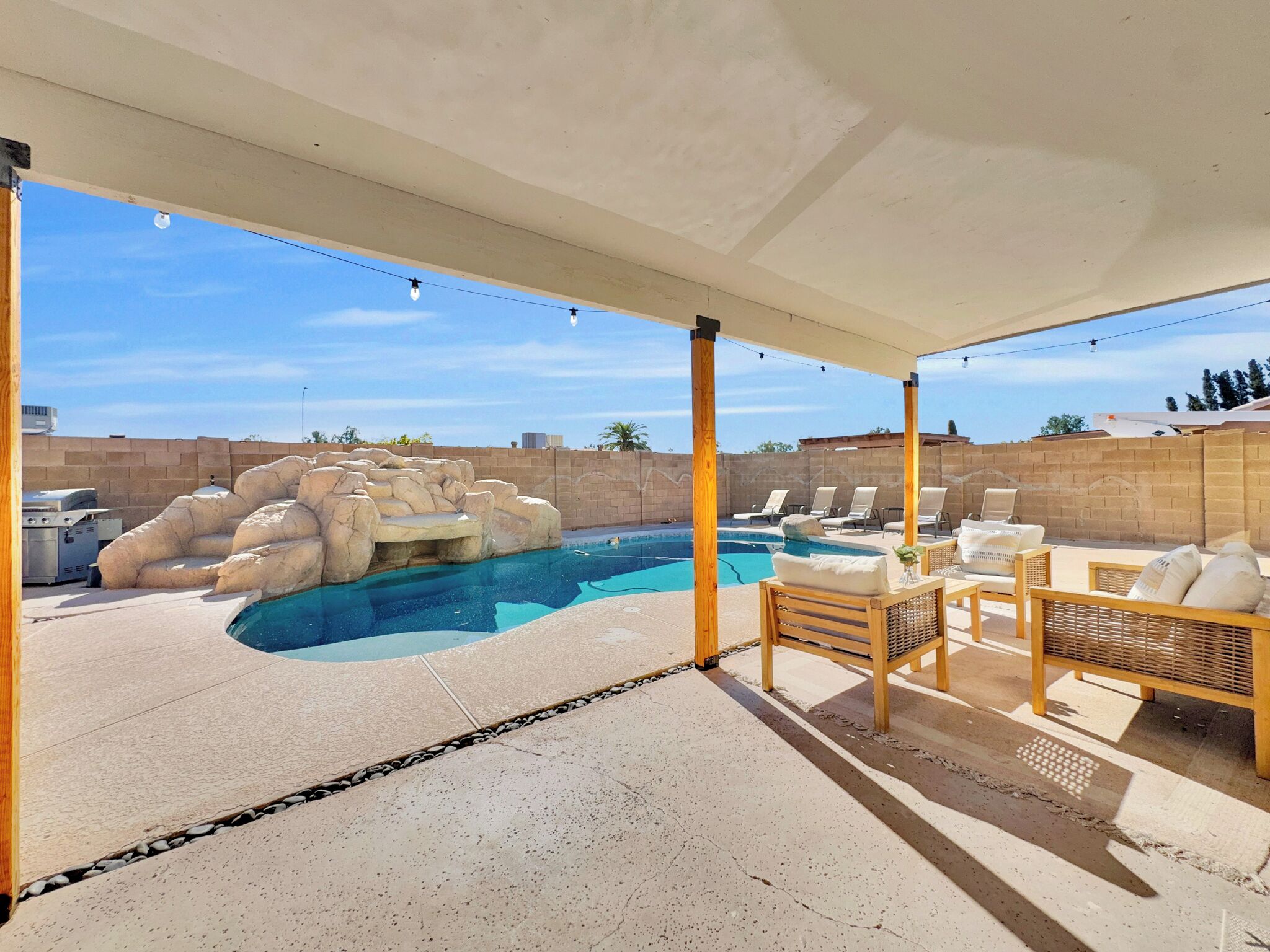 A covered outdoor area with a pool, lounge chairs, and a barbecue grill.