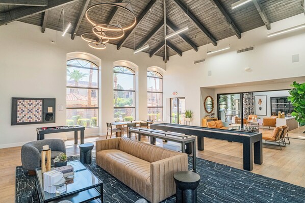 A spacious living area with a pool table, sofa, and coffee table. There are large windows providing natural light and views of the outside.