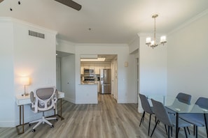 A modern kitchen with stainless steel appliances, a dining area with a glass table and chairs, and a workspace with a desk and office chair. - San Portella (Tempe)