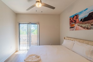 A bedroom with a bed, a ceiling fan, a window with blinds, and a painting on the wall. - San Portella (Tempe)