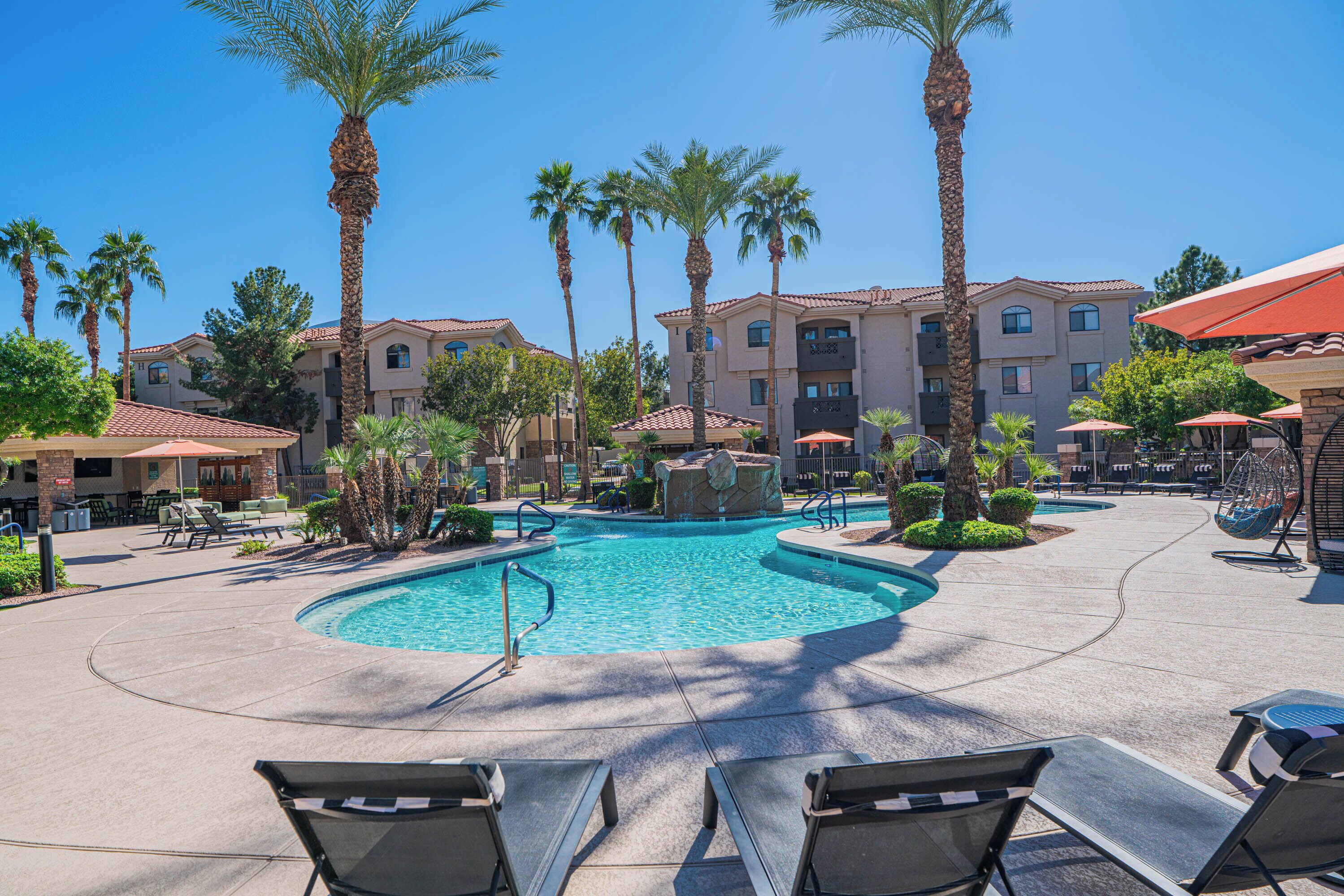A pool area with lounge chairs, palm trees, and a building with multiple balconies.
