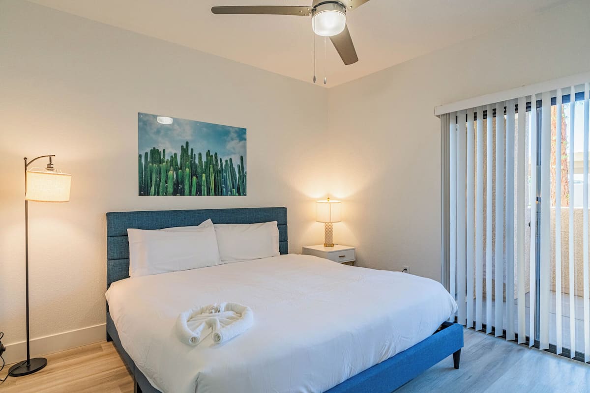 Un letto rifatto con lenzuola bianche, una testiera blu e un quadro con dei cactus al muro.