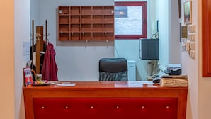 Een receptiebalie met een rode bekleding, een kroonluchter erboven en een raam met zonwering op de achtergrond.