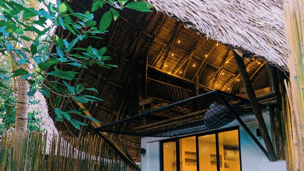 Een modern huis met rieten dak, grote ramen en een balkon.