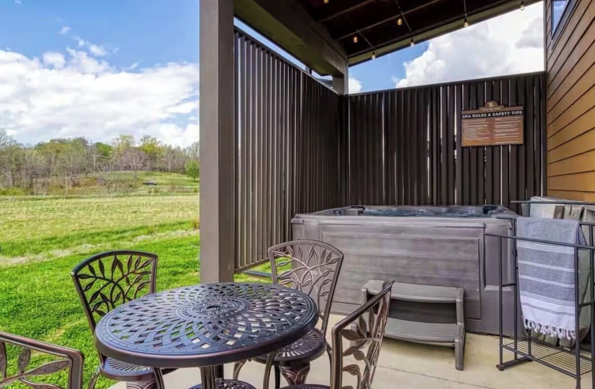 An outdoor patio with a hot tub, metal chairs, and a table.