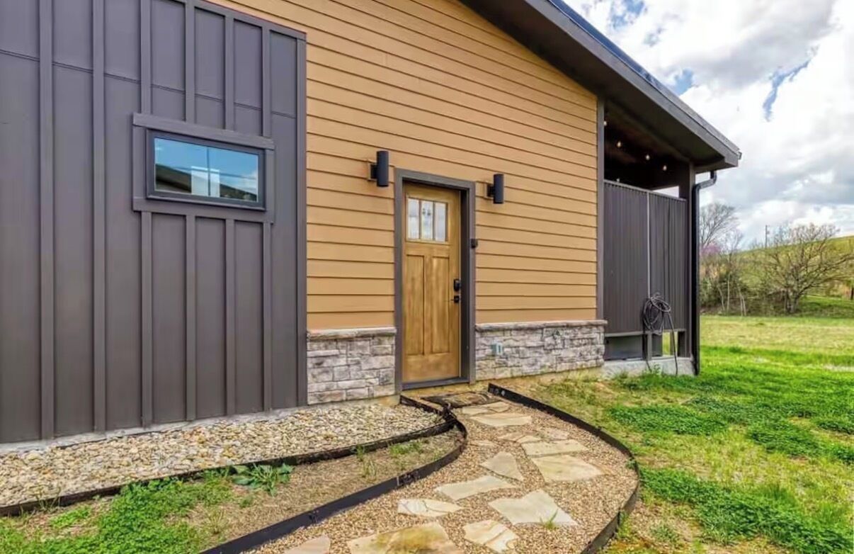 Une maison moderne avec une porte en bois, des marches en pierre et un chemin de gravier menant à l’entrée.