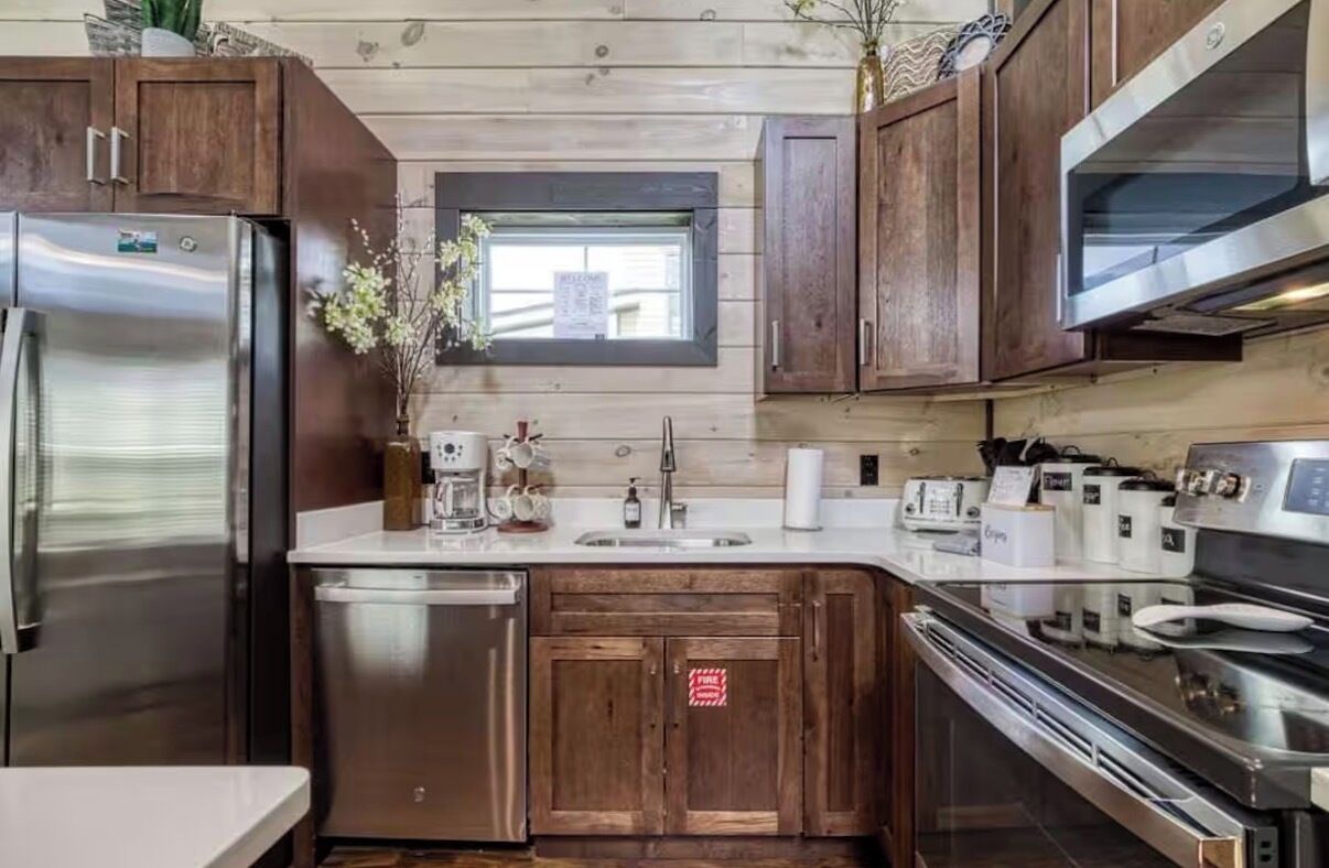 A modern kitchen with wooden cabinets, stainless steel appliances, and a small window.