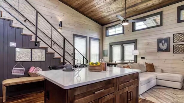A spacious kitchen with a large island, wooden cabinets, and a staircase leading to another level. - Peaceful cabin retreat near all you want to do in the Smokey Mountains! (Sevierville)