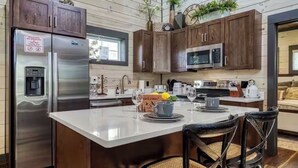 A modern kitchen with wooden cabinets, stainless steel appliances, and a central island with chairs. - Peaceful cabin retreat near all you want to do in the Smokey Mountains! (Sevierville)
