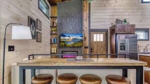 A wooden cabin interior with a kitchen area, a bar with stools, and a fireplace. - Peaceful cabin retreat near all you want to do in the Smokey Mountains! (Sevierville)