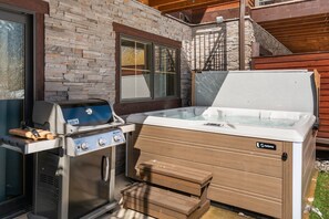 An outdoor kitchen with a grill, a hot tub, and a wooden deck. - Modern Big Sky Retreat  | Hot tub + Shared Pool (Big Sky)