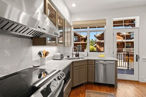A modern kitchen with a built-in oven, a dishwasher, and a large window overlooking a wooden deck. - Modern Big Sky Retreat  | Hot tub + Shared Pool (Big Sky)
