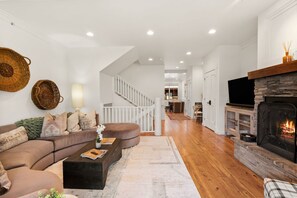 A modern living room with a fireplace, a sofa set, and a staircase leading to an upper level. - Modern Big Sky Retreat  | Hot tub + Shared Pool (Big Sky)
