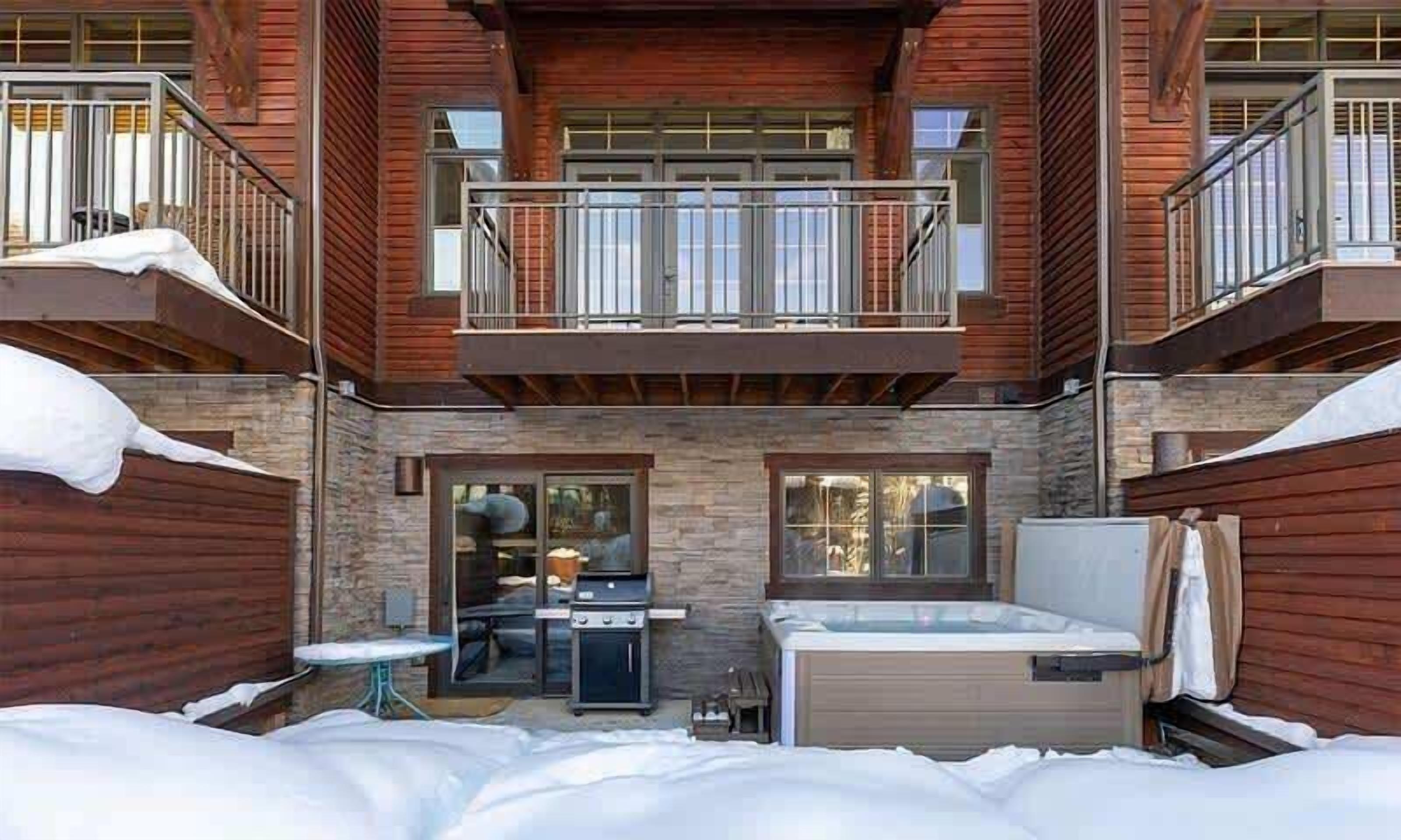 A two-story log cabin with a stone fireplace, a hot tub, and a covered patio area.
