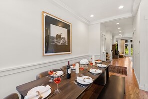 A dining area with a long table set for a meal, a framed picture on the wall, and a view into another room. - Modern Big Sky Retreat  | Hot tub + Shared Pool (Big Sky)