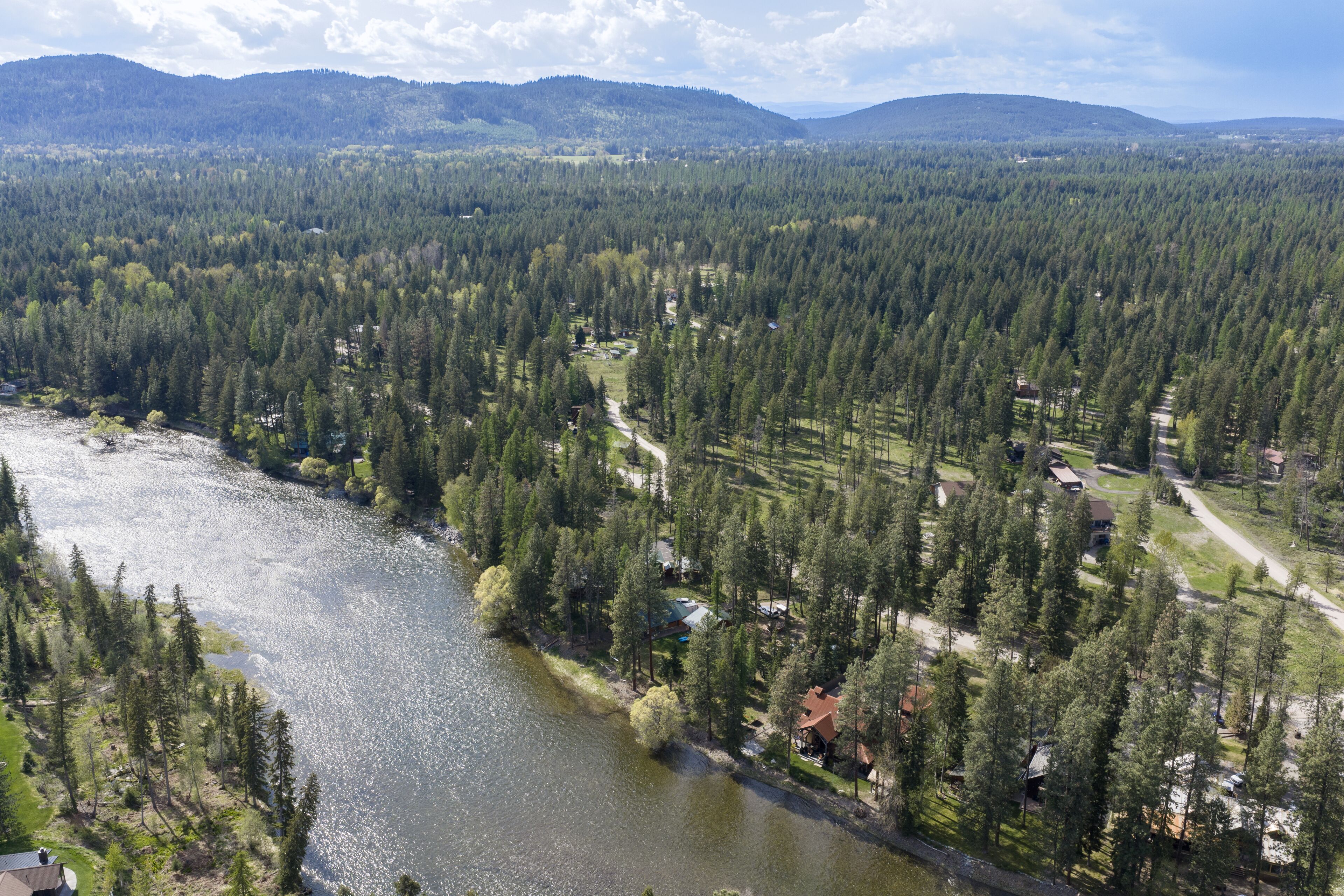 Un río rodeado de bosque denso y casas con senderos visibles.
