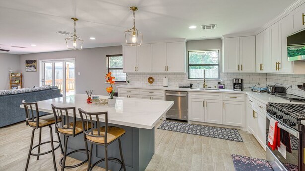 A modern kitchen with white cabinets, a central island with bar stools, a dishwasher, and a stove. - Charming 4-bedroom 2.5 Bath one level house with garage 7 miles from NRG stadium (Houston)