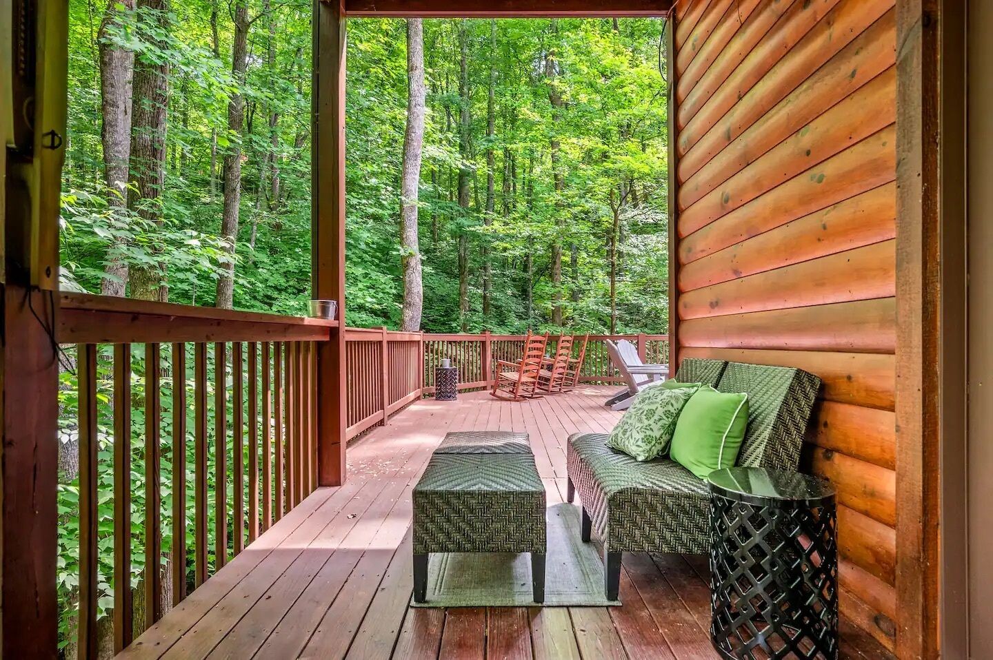 Eine Holzterrasse mit einer Couch und Sesseln, umgeben von einem Wald.
