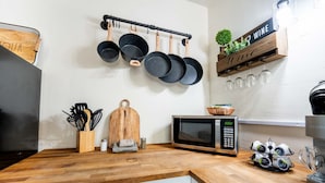 A kitchen with a wooden countertop, a hanging pot rack, a microwave, and a wine sign. - Cozy 2BR W/ Desk • Fast Wi-Fi • Easy Parking (Tucson)
