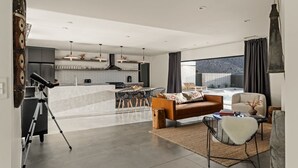 A modern living room with a sofa, a coffee table, and a dining area with chairs. - Celestine - Modern w Pool Near Park Entrance (Joshua Tree)