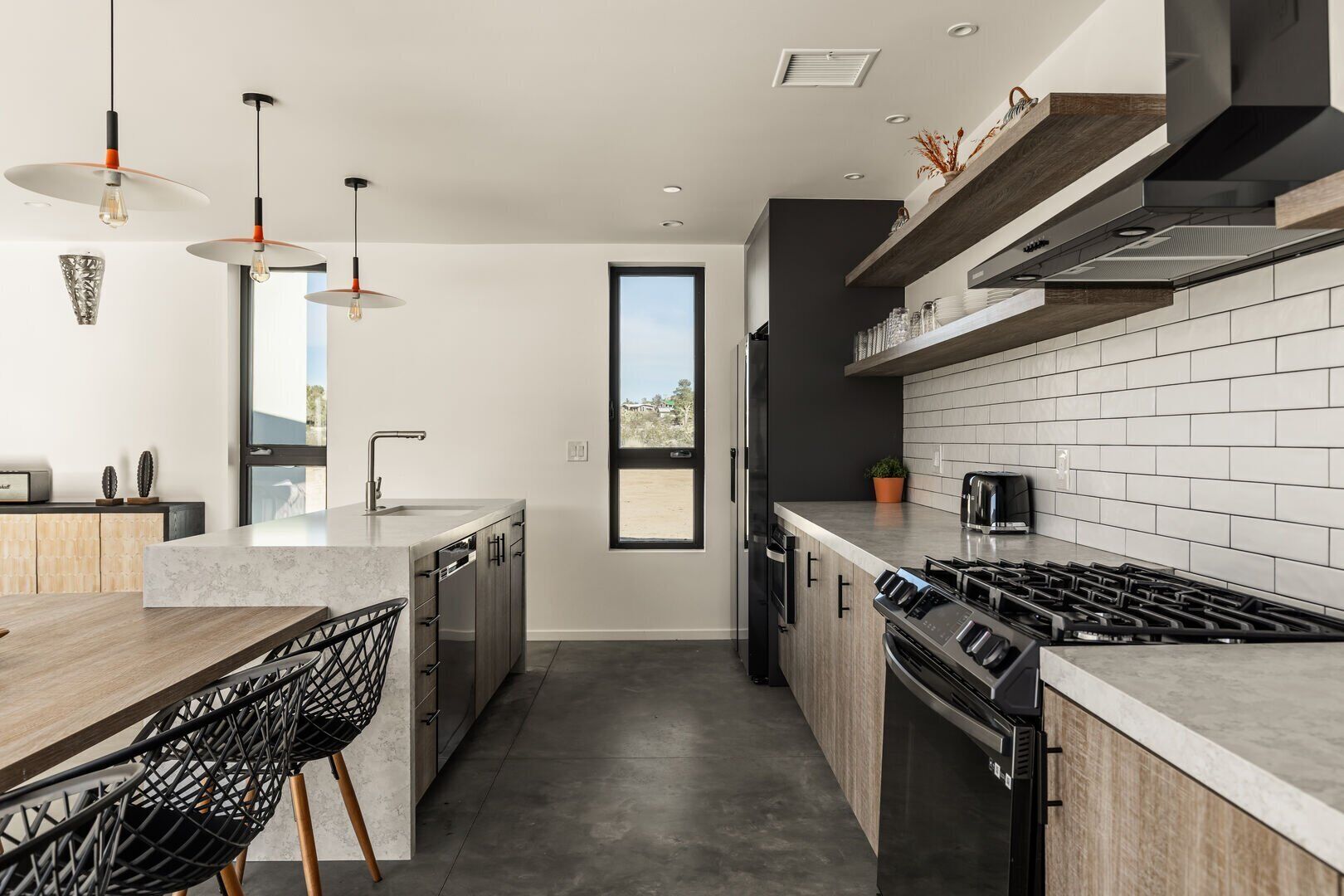 A modern kitchen with a large island, stainless steel appliances, and a view through a window.