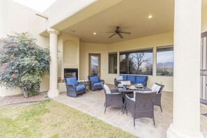 An outdoor patio with wicker furniture, a fireplace, and large windows. - Luxe Tuscan Villa - Organ Mtn Views, Patio Living, Sonoma Golf (Las Cruces)