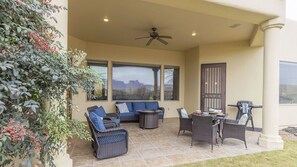 A covered patio area with wicker furniture, a ceiling fan, and a view of the city through large windows. - Luxe Tuscan Villa - Organ Mtn Views, Patio Living, Sonoma Golf (Las Cruces)