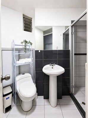 Ein modernes Badezimmer mit Toilette, Waschbecken und einer Metallregaleinheit mit einer Pflanze.