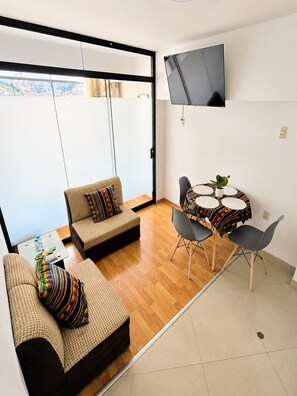 Ein modernes Wohnzimmer mit einer Couch, Sesseln, einem kleinen Tisch und einem an der Wand befestigten Fernseher.
