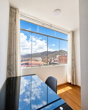 Ein Zimmer mit großem Fenster, einem Glastisch, einem Stuhl und Holzboden.