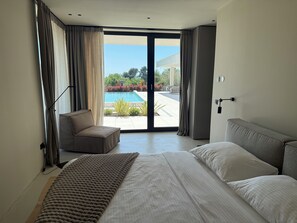 A modern bedroom with a large bed, a chair, and a view of a swimming pool. - Villa Lavis (Istria - Sveti Lovreč) (Sveti Lovreč)