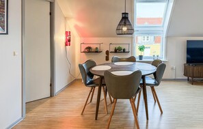 Ein moderner Essbereich mit einem runden Tisch, sechs Stühlen, einer Pendelleuchte und Blick auf ein Gebäude durch ein Fenster.