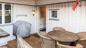 A cozy outdoor seating area with wicker furniture and a wooden table, a barbecue grill, and a flag on the wall. - 2 bedroom amazing apartment in Gudhjem (Gudhjem)