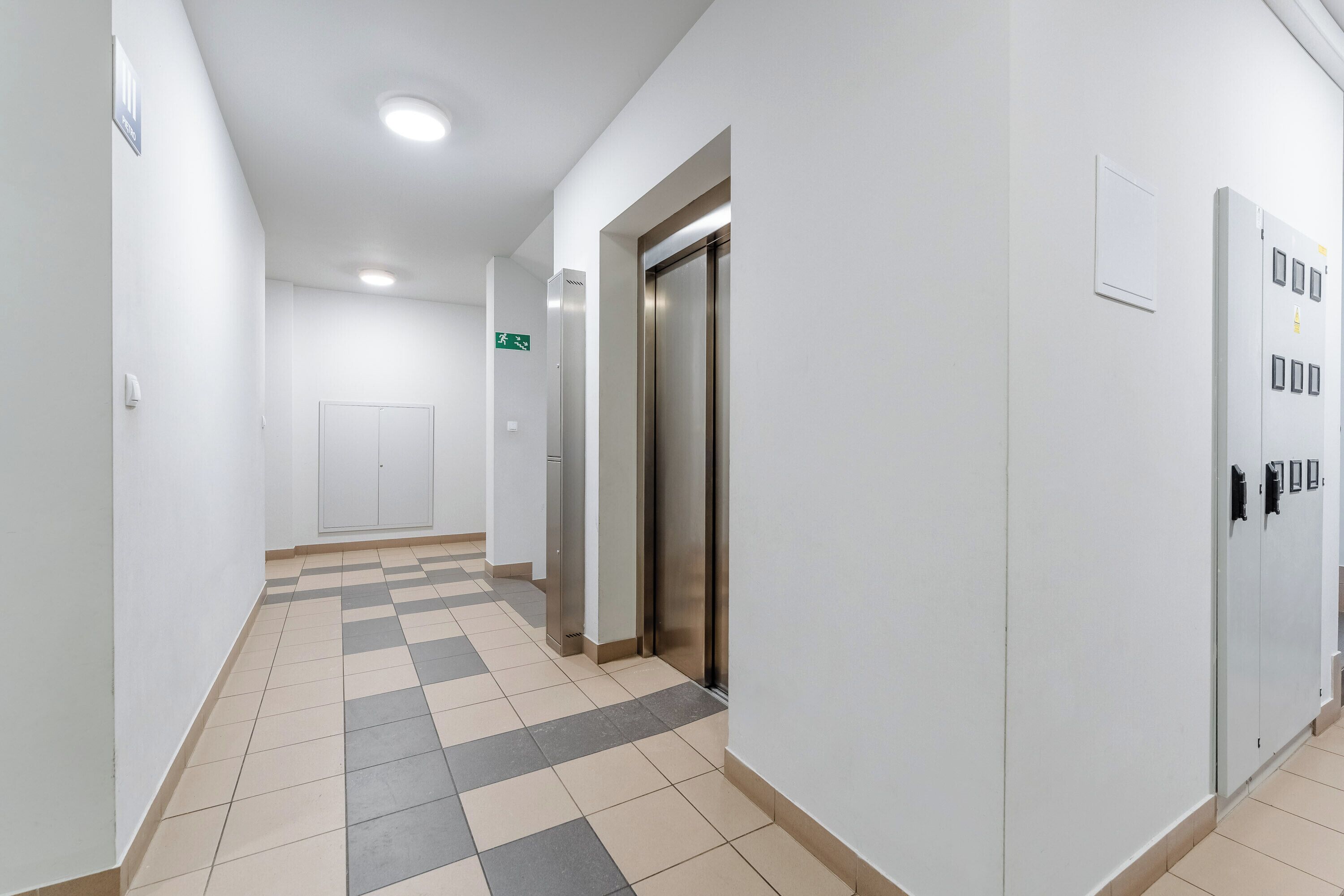 Ein aufgeräumter, moderner Flur mit einem Schachbrettmuster auf dem Boden, einer Tür mit Griff und einer Wandleuchte.